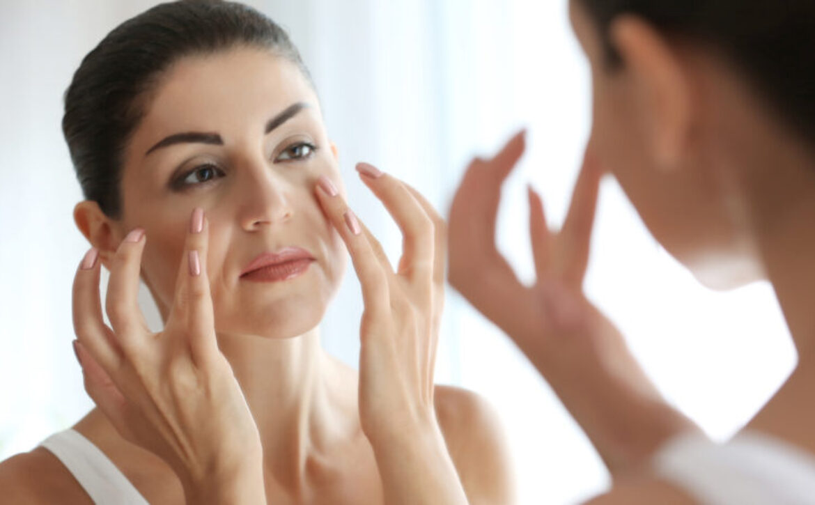 Adult woman checking her face in mirror on light background